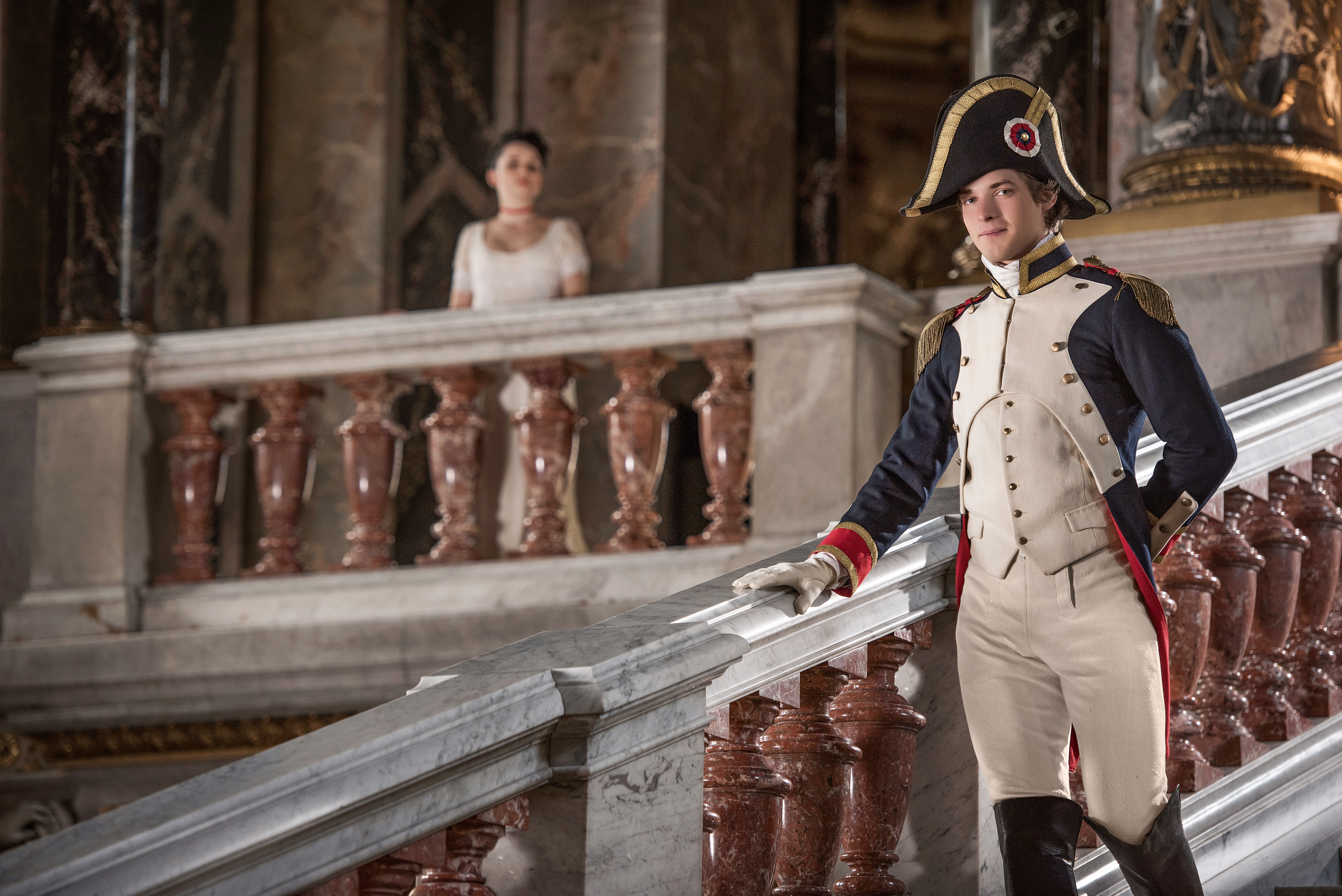 napoleonic and empire era inspired advertising photo shoot in khm vienna by art director and fashion stylist katalina sasdy. a soldier in french, napoleonic uniform is going down the stairs in the palace. his lady in a white empire dress is waiting for him on the terrace in the background.