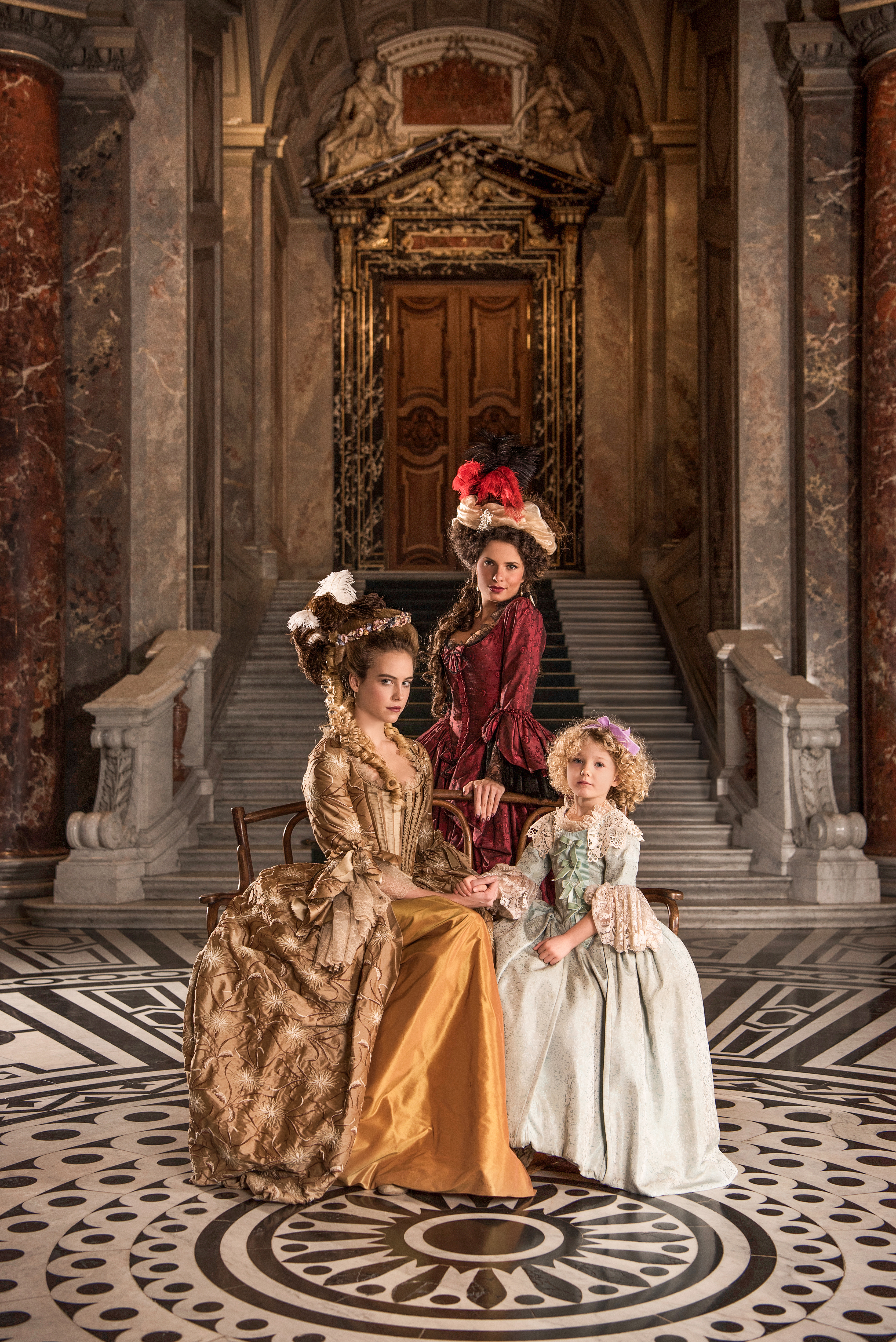 vivienne westwood inspired advertising photo shoot in khm vienna by art director and fashion stylist katalina sasdy. marie antoinette is sitting on a sofa in a yellow silk dress with her little daughter marie therese. behind them stands the queens best friend, princess lamballe, in a red dress. all are looking into the camera.
