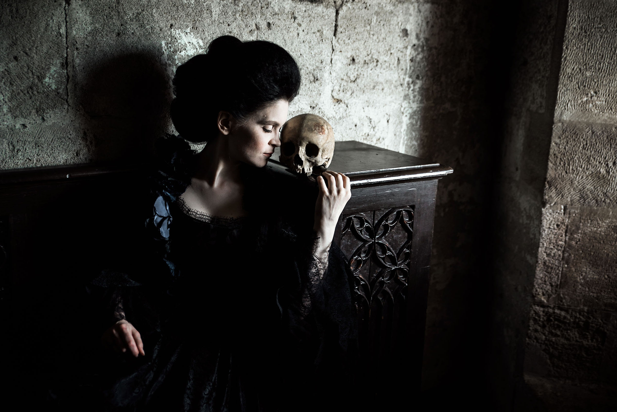 rokoko inspired halloween advertising photo shoot at the castle of liechtenstein by fashion historian and stylist katalina sasdy. a lady in dark 18th century costume is leaning against an embellished counter on which a skull lies. her hair is pinned up in rococo style.