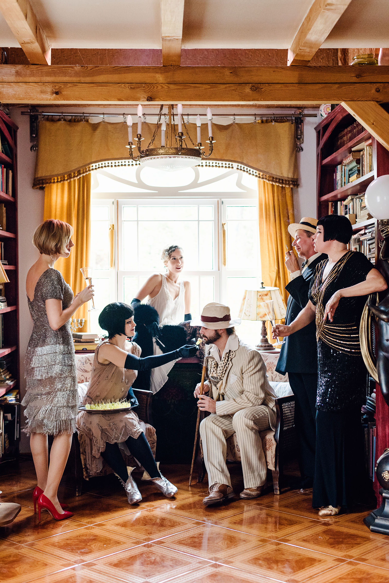the great gatsby inspired wedding party photo shoot by vintage fashion stylist katalina sasdy. a group of six people toasting a party with champagne glasses. everyone is dressed in the style of the 1920s. the ladies are wearing white, light pink, silver and black evening dresses with gloves and fur stoles. the gentlemen are wearing creme and black suits with beige hat and black walking stick.
