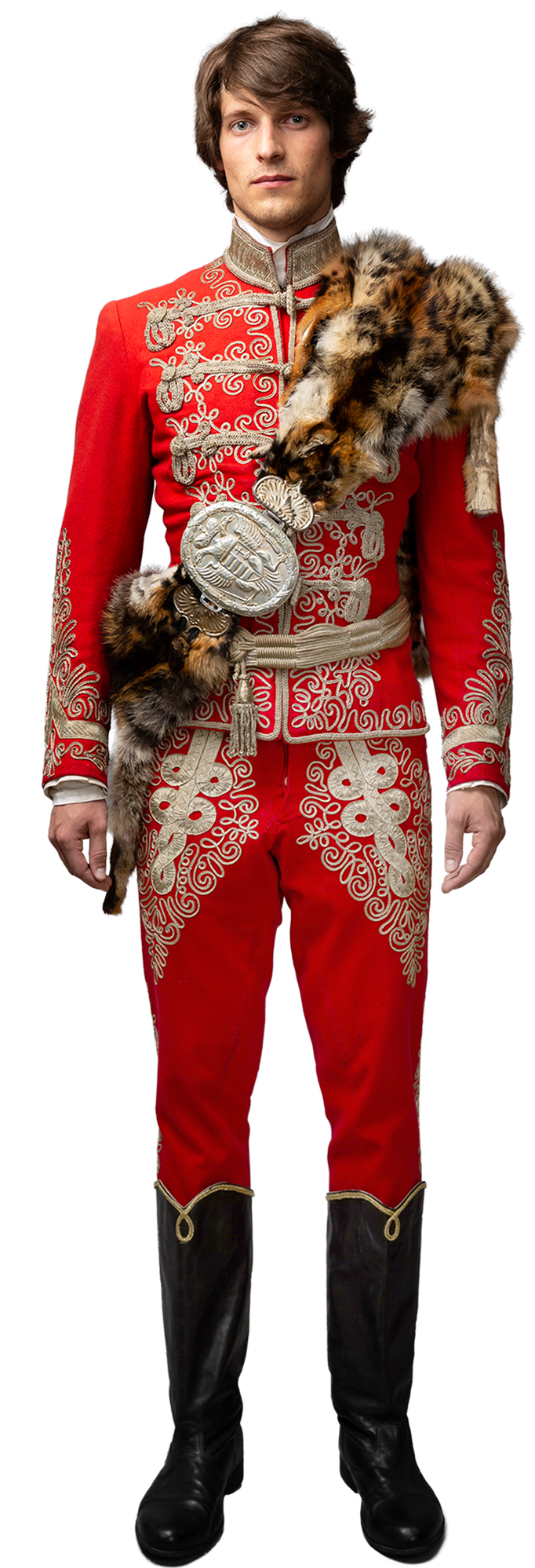 1848 hungarian revolution inspired advertising photo shoot by fashion stylist katalina sasdy. a genteman is wearing a red hussar uniform with a panther skin that is held together with a silver buckle. the uniform includes a belt, braided from silver thread, silver embroidery, uniform decorations and black boots. it is a full-body picture and the hussar is looking straight into the camera.