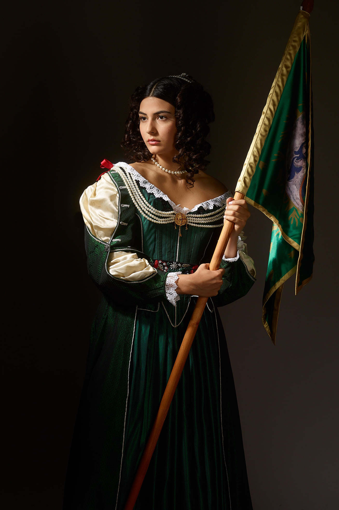 hungarian freedom fighters inspired museum photo shoot by fashion historian and stylist katalina sasdy. helena zrinski is wearing a green silk dress in the style of the 17th century in hungary. the dress is decorated with beads, red ribbons and lace. the parts of the silk blouse are open on her sleeves. she carries the flag of her son, the hungarian freedom fighter, prince francis rakoczi II. she is looking resolutely into the camera.