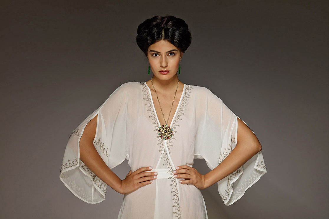 galerie zacke auction house advertsing photo shoot by fashion historian and stylist katalina sasdy. the model is wearing a white kaftan dress with silver embroidery by nasty gal. her black hair is braided and pinned up on the top of her head. she is promoting an antique white gold necklace and malachite earrings.