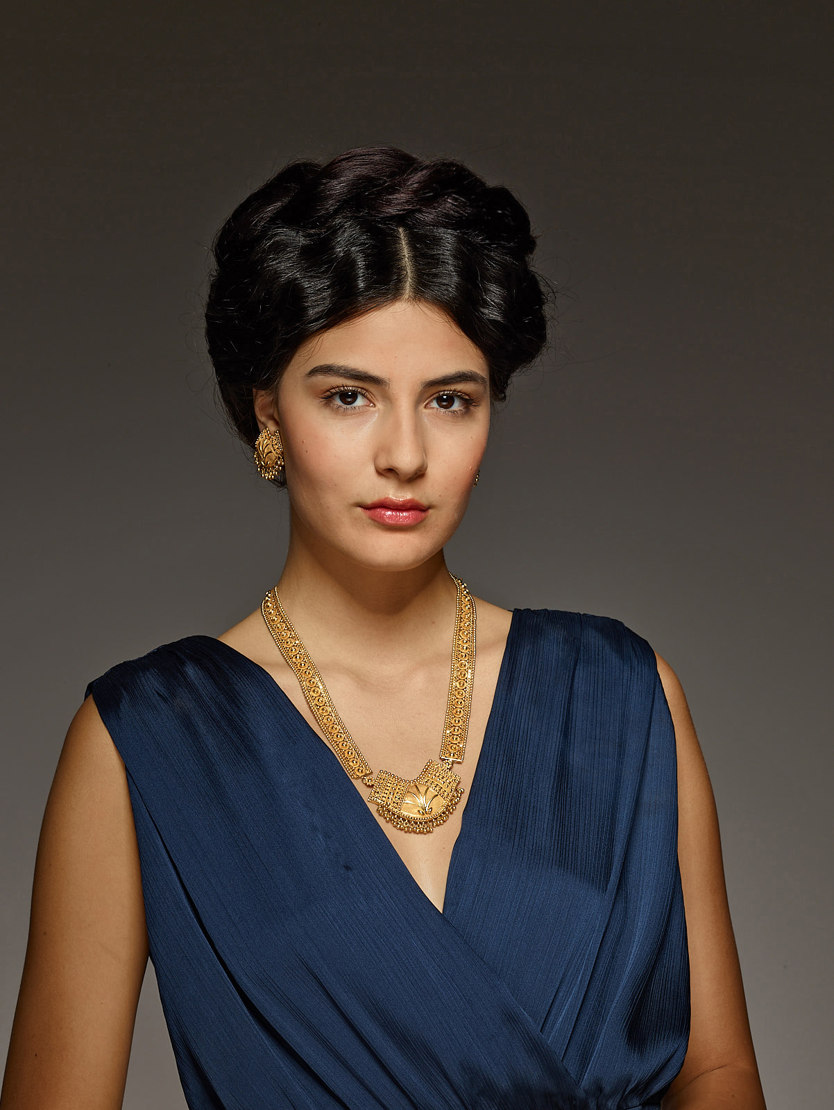 galerie-zacke-auction-house-advertsing-photo-shoot-by art director and fashion stylist katalina sasdy. the model is wearing a dark blue silk jumpsuit. her black hair is braided and pinned up on the top of her head. she is promoting a thousand year old asian gold necklace and earrings.