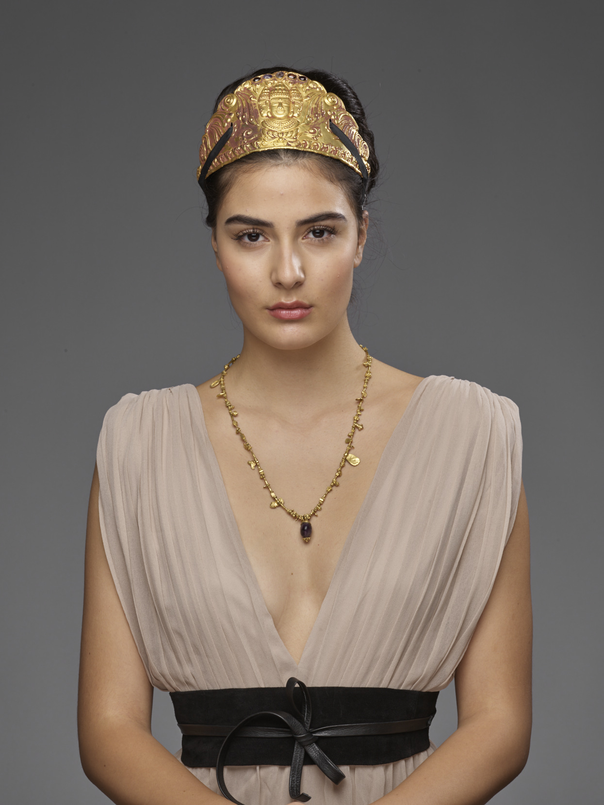 galerie zacke auction house advertsing photo shoot by vintage fashion stylist katalina sasdy. the model is wearing a light beige, low-cut dress with a black leather obi belt. her black hair is pinned up in a high bun. she is promoting a thousand year old asian gold tiara and necklace.