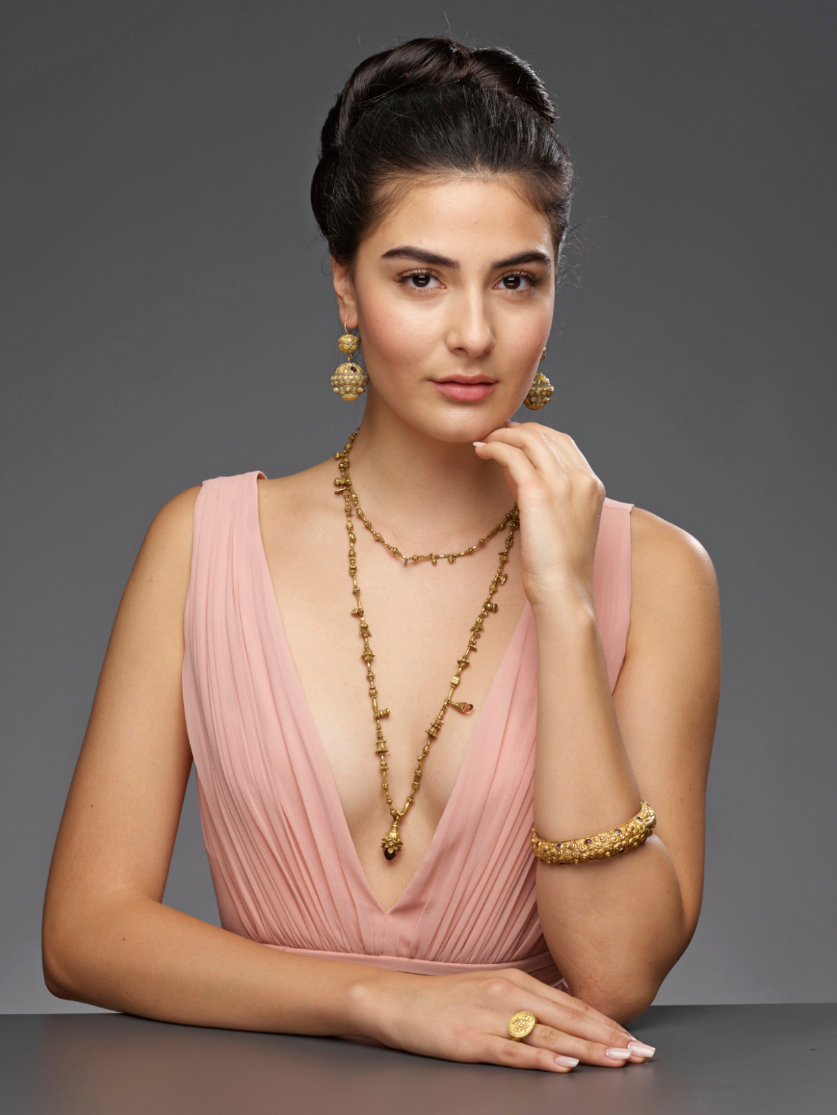 galerie zacke auction house advertsing photo shoot by fashion stylist katalina sasdy. the model is wearing a pink, low-cut dress. her black hair is pinned up in a high bun. she is promoting a thousand year old asian gold necklace, bracelet and ring.